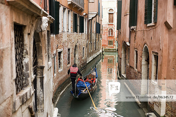 A gondola boat gliding down a small narrow waterway  between historic houses in the city of Venice.