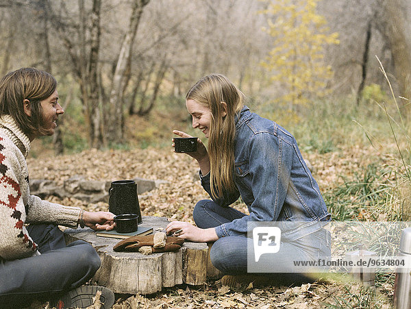 Smiling couple sitting on the ground in a forest  drinking coffee.