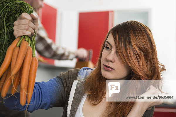Young woman looking at bunch of carrots in kitchen