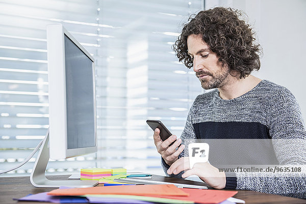 Businessman working on computer and text messaging on mobile phone