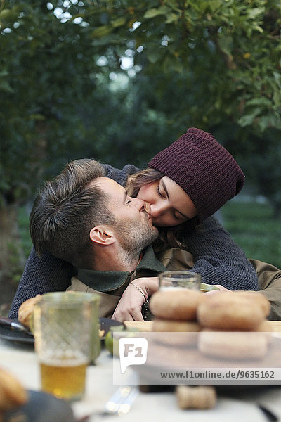 An apple orchard in Utah. A couple kissing  food and drink on a table.