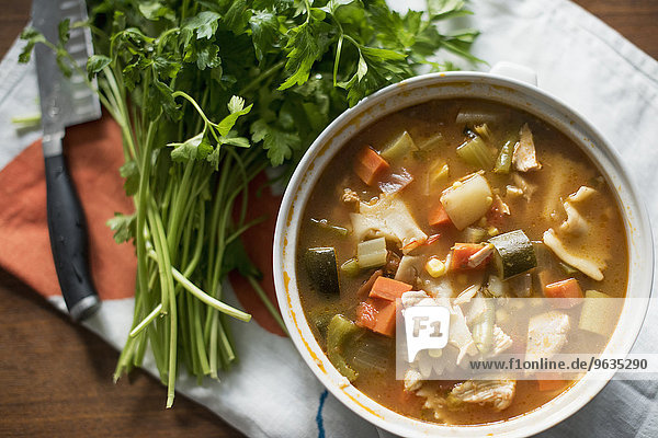 A bowl of vegetable stew and a bunch of fresh herbs on a table.
