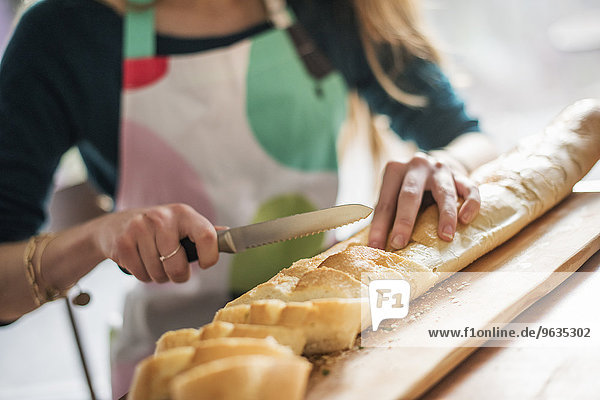 Close up of a woman wearing an apron  sitting at a table  slicing a baguette.