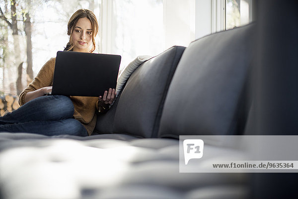 Woman sitting on a sofa looking at her laptop  smiling.