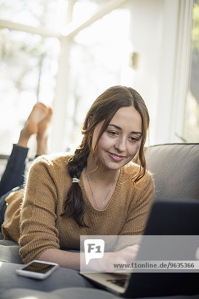 Woman lying on a sofa looking at her laptop  smiling.