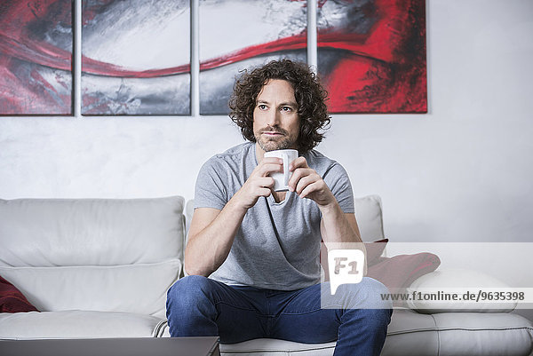Man sitting on couch and drinking cup of coffee