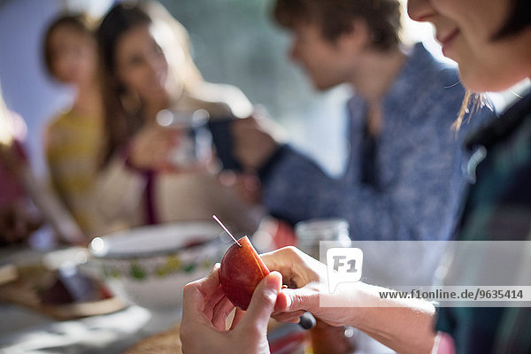 A group of people sitting at a table  eating and chatting. A woman slicing an apple.