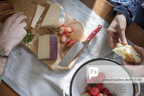 Man and woman sitting at a table with a wooden chopping board with a selection of cheeses  strawberries and bread.