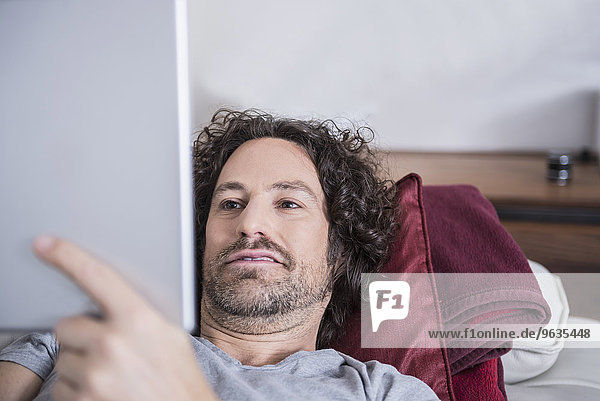 Man lying down on couch and using a digital tablet