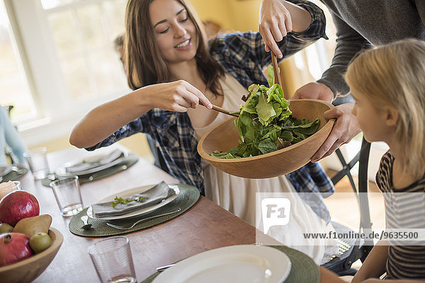 A young woman helping herself to salad at a table.