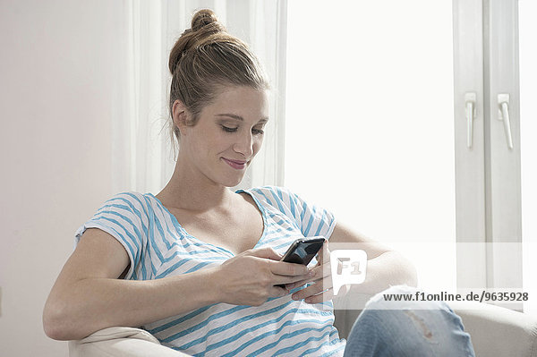 Attractive young blond pregnant woman typing SMS
