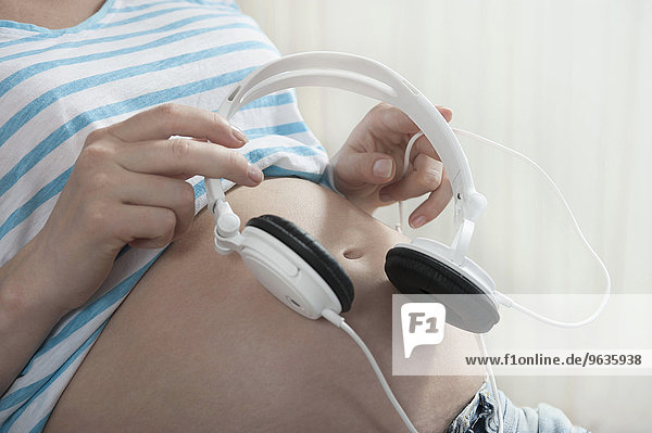 Close up pregnant woman holding headphones stomach