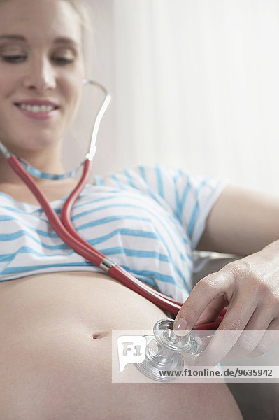 Pregnant woman holding stethoscope stomach