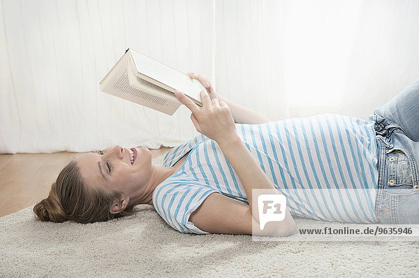Young pregnant woman lying carpet reading book