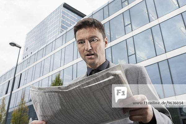 Businessman looking shocked while reading newspaper
