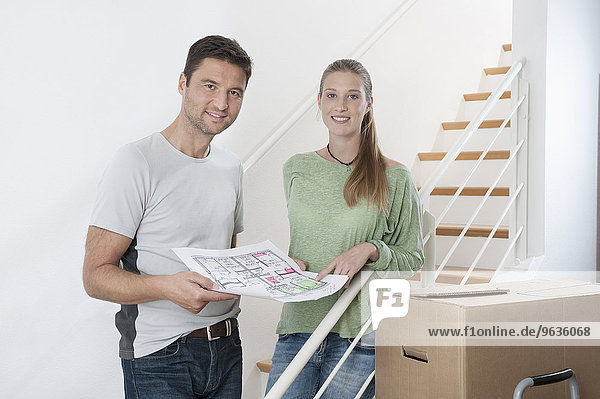 Couple discussing a blueprint by staircase in new home