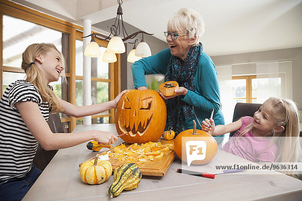 Senior woman carving pumpkin for Halloween with her granddaughters