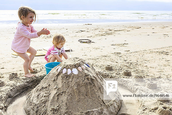 Two girls  toddlers  playing with a sand castle on the beach  Langstrand  Namibia  Africa