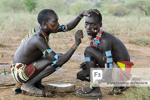 'Men from the Hamar tribe painting each other for the initiation ritual ''leap over the cattle''  southern Omo valley  Ethiopia  Africa'