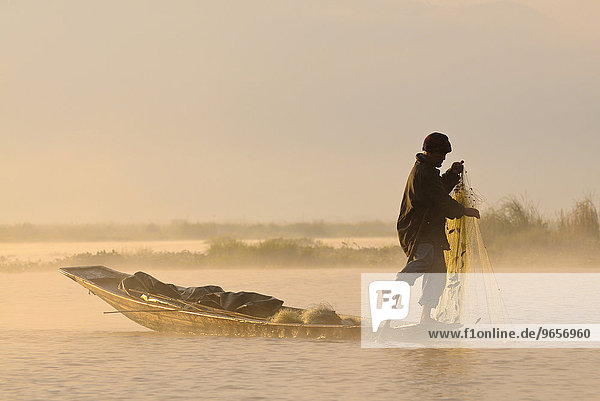 Leg rower  fisherman in a traditional canoe in the morning light  Inle Lake  Myanmar  Burma  Southeast Asia  Asia