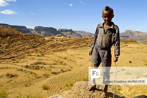 Black boy with a mohawk hairdo standing in front of the barren landscape of northern Ethiopia  Ethiopia  Africa