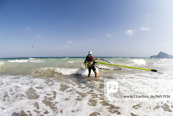 Windsurfer wearing helmet carrying his surfboard into the sea  Mediterranean coast  Spain  Europe