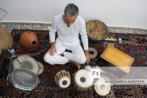Musician in his early 40's  sitting amongst his percussion instruments  in front of him tablas  a north Indian percussion instrument  beside him a box drum known as a Cajon