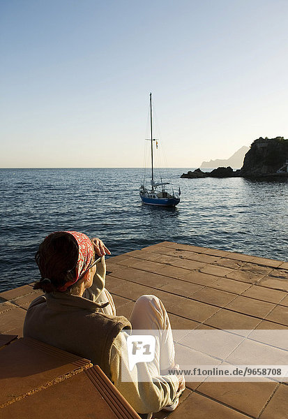 Frau schaut auf ein Segelboot in einer Bucht an der spanischen Mittelmeerküste nahe Altea  Costa Blanca  Spanien  Europa