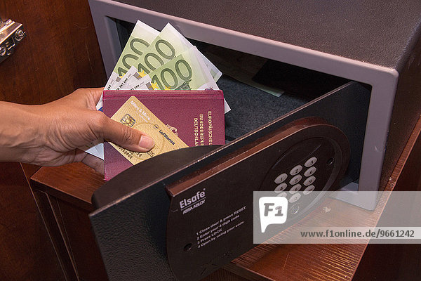Geöffneter Tresor  Hand hält Kreditkarte  Reisepass und Bargeld  in einem Hotelzimmer