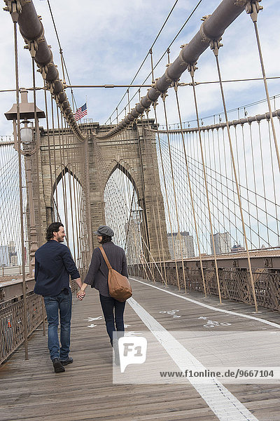 Couple holding hands and walking on Brooklyn Bridge