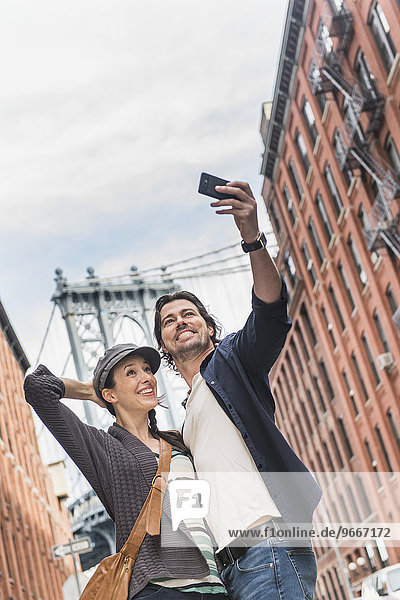 Couple taking selfie on street  Brooklyn Bridge in background