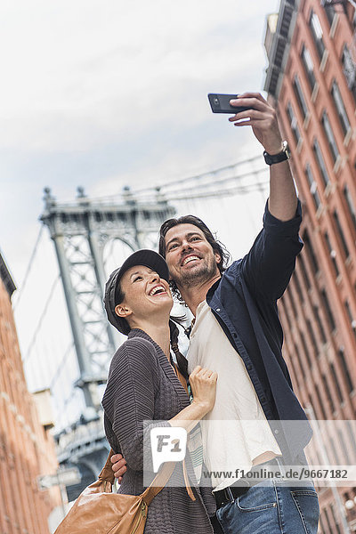 Couple taking selfie on street  Brooklyn Bridge in background