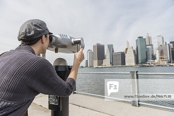 Woman watching cityscape through coin-operated binoculars