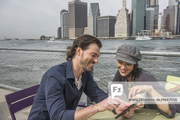 Happy couple sitting and using tablet pc with cityscape in background