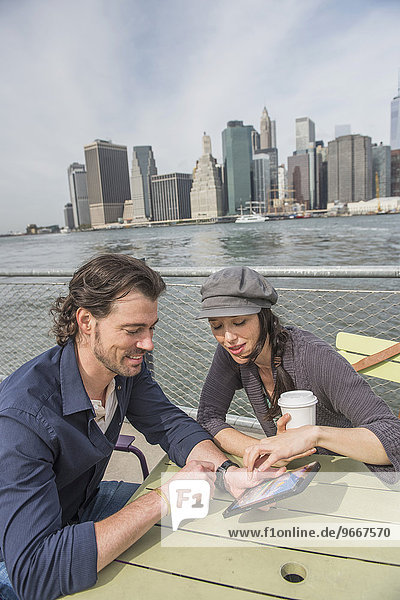 Happy couple sitting and using tablet pc with cityscape in background