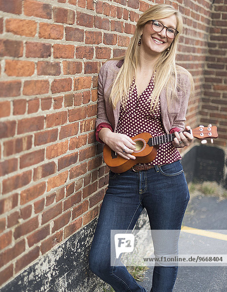 Woman standing against brick wall and playing ukulele