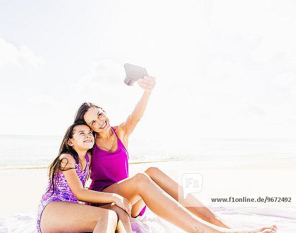 Mom taking picture with her daughter (6-7) on beach