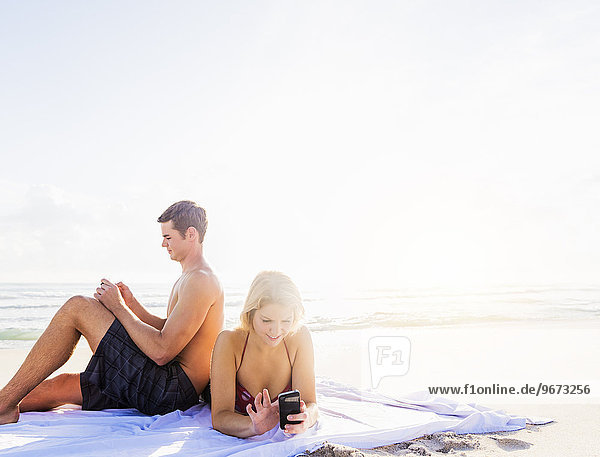 Portrait of young couple relaxing on beach  using smart phones