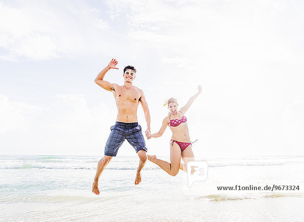 Young couple jumping on beach  holding hands