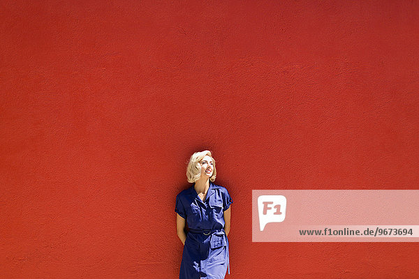 Woman in blue dress posing against red wall in sunlight