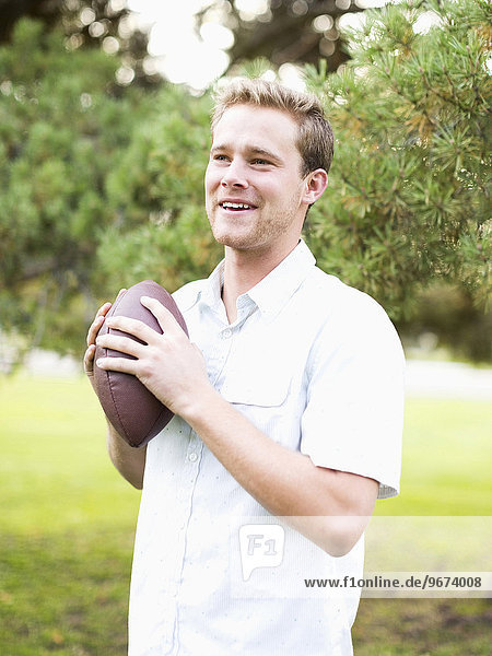 Portrait of young man holding football in park