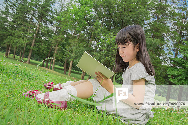 Japanese kid sitting on grass with a book in a park