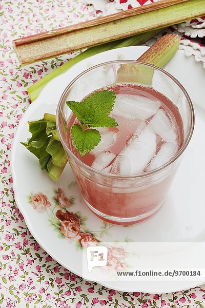 Ein Glas Rhabarberschorle mit Eiswürfeln und Rhabarberstücken auf altem Rosenteller