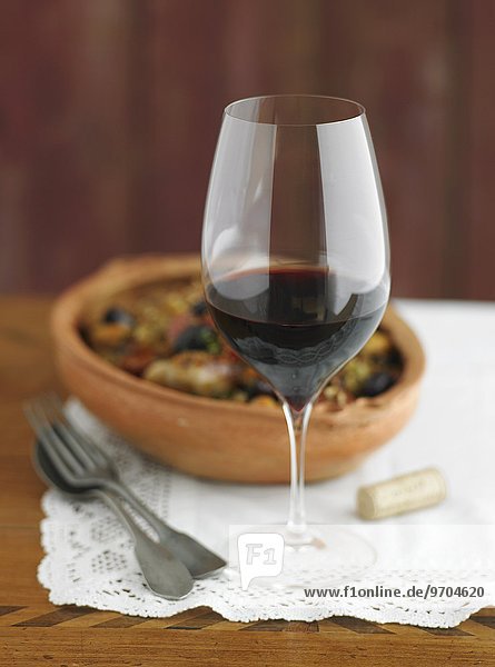 'Rotweinglas; im Hintergrund Tapas in einer Terrakottaschale'
