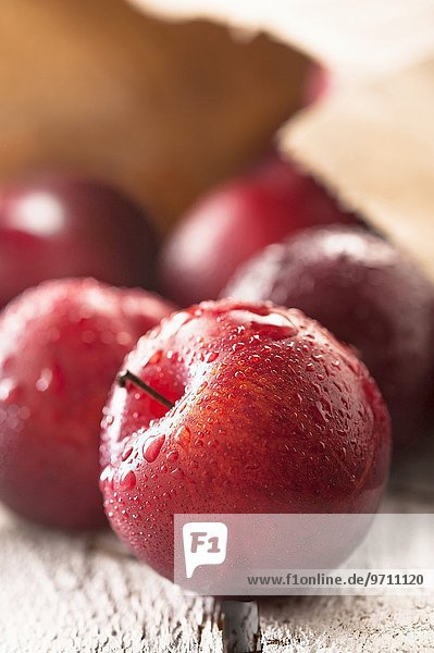 Freshly washed red plums with a paper bag in the background