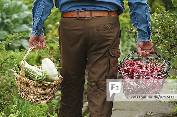 A man carrying two baskets of freshly harvested vegetables in from the garden