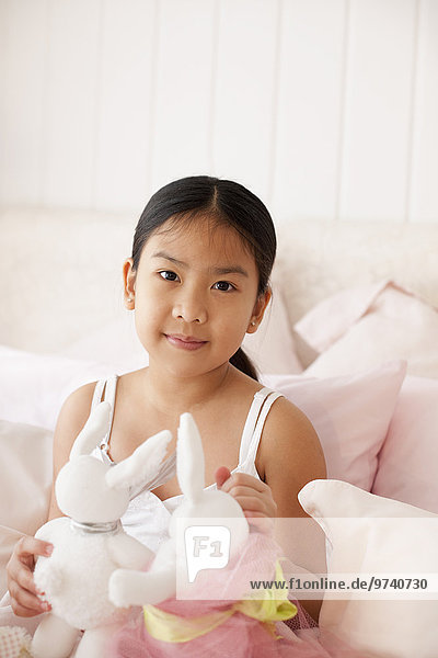 Asian girl on bed holding stuffed rabbits