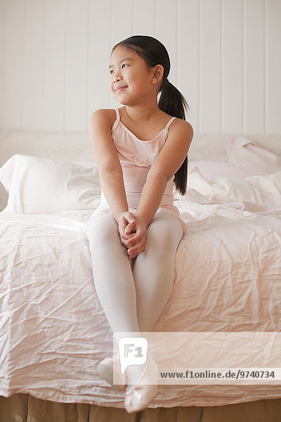Asian girl in ballet costume sitting on bed