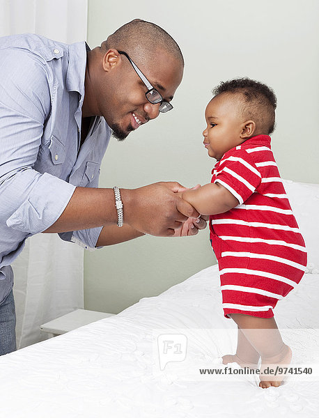 African American father helping baby son to stand up