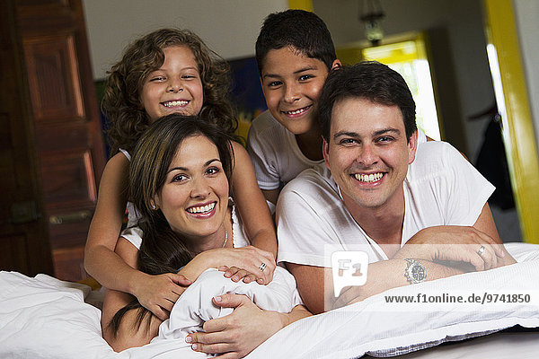 Smiling Hispanic family laying on bed together